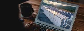 Laptop screen displays a row of battery storage units next to solar panels in a landscape.
