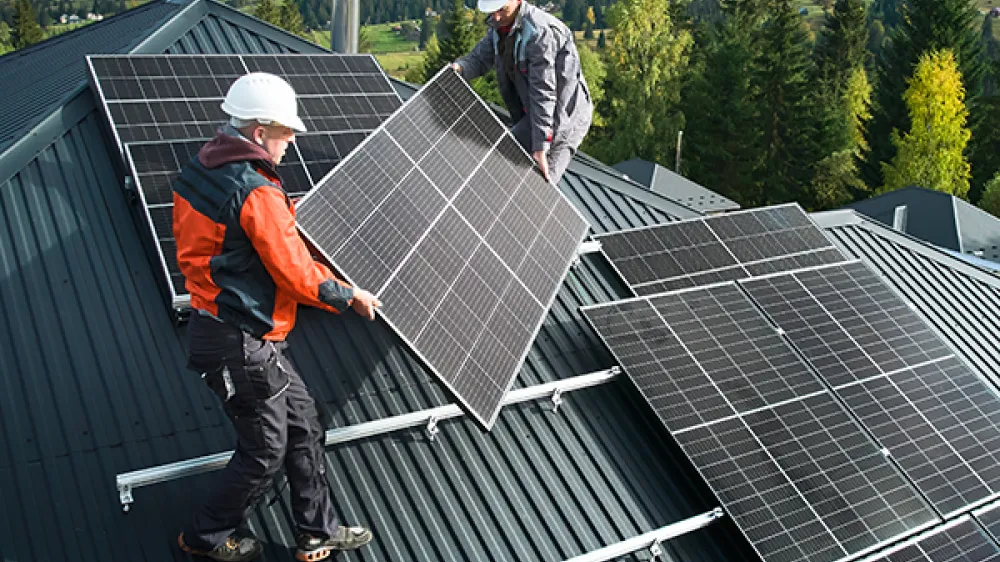Two workers are installing solar panels on the roof of a house.