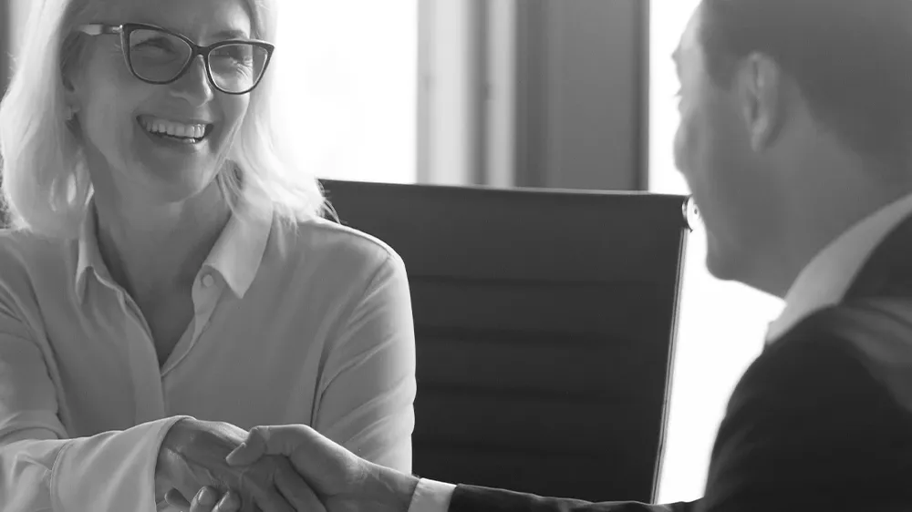 Smiling woman in glasses shaking hands with a man in an office setting.
