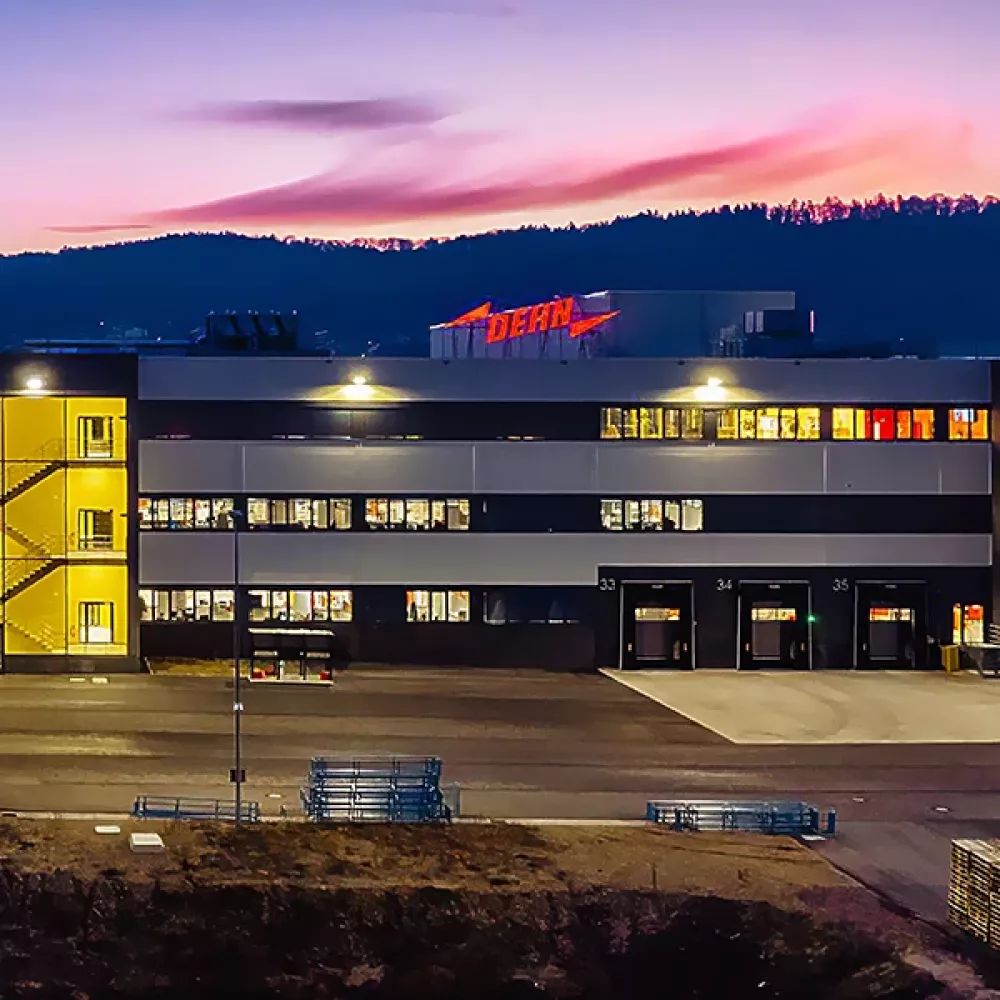 Industrial building with 'DEHN' sign lit in red at dusk, reflecting in a pond in the foreground