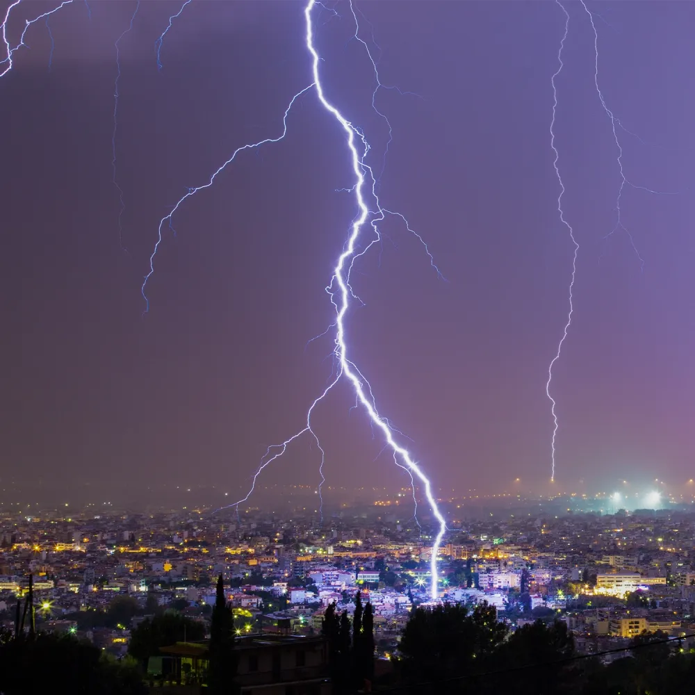 A bright lightning bolt striking a city at night, illuminating buildings under a purple sky.