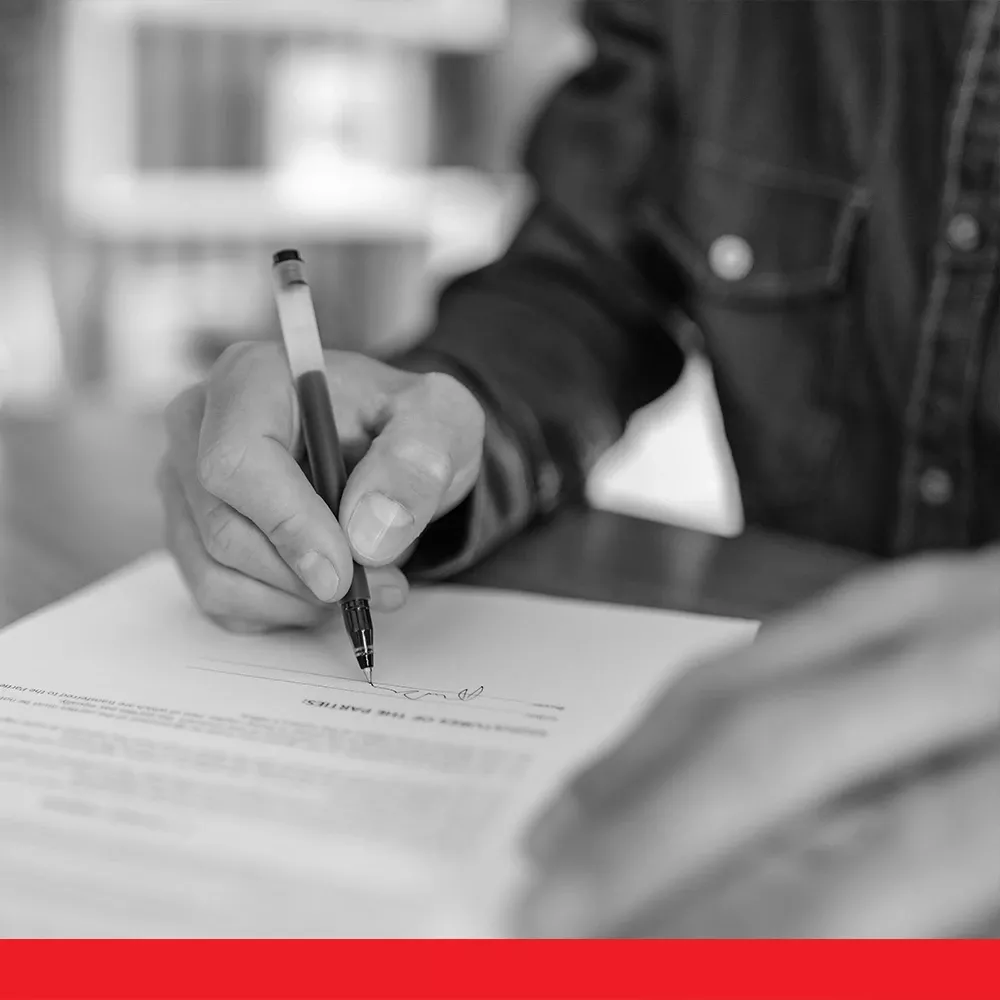 Person signing a document with a pen at a desk in a close-up view.