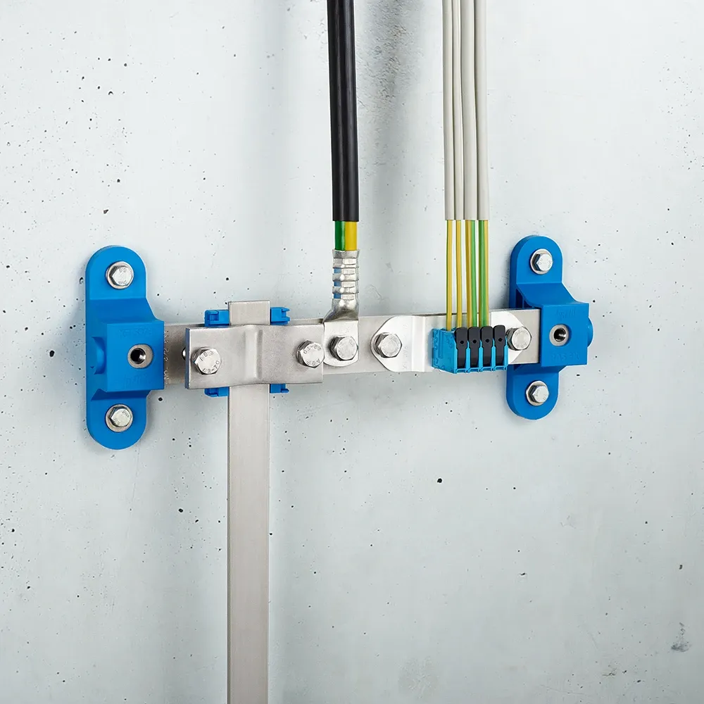 Wall-mounted grounding bar with metal clamps, connected cables, and blue mounting brackets on a light gray wall.