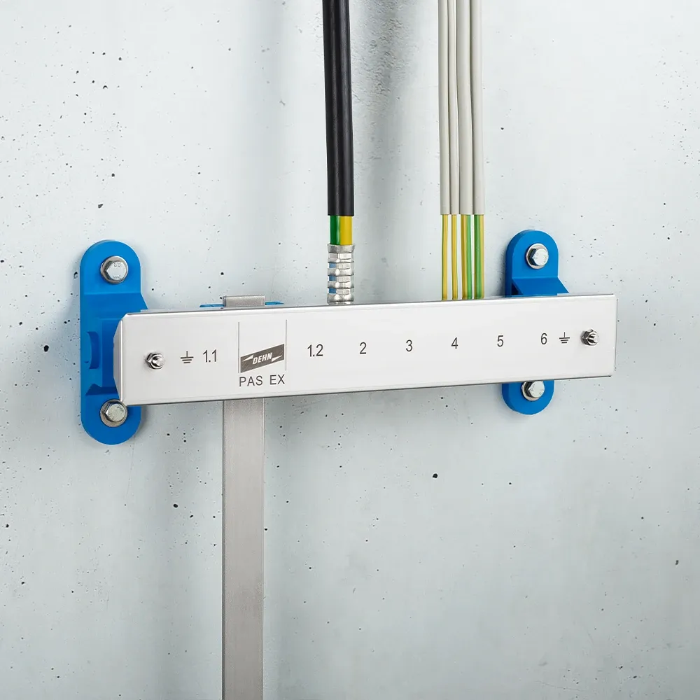 Wall-mounted grounding bar labeled "PAS EX" with numbered terminals and connected cables on a light gray wall.
