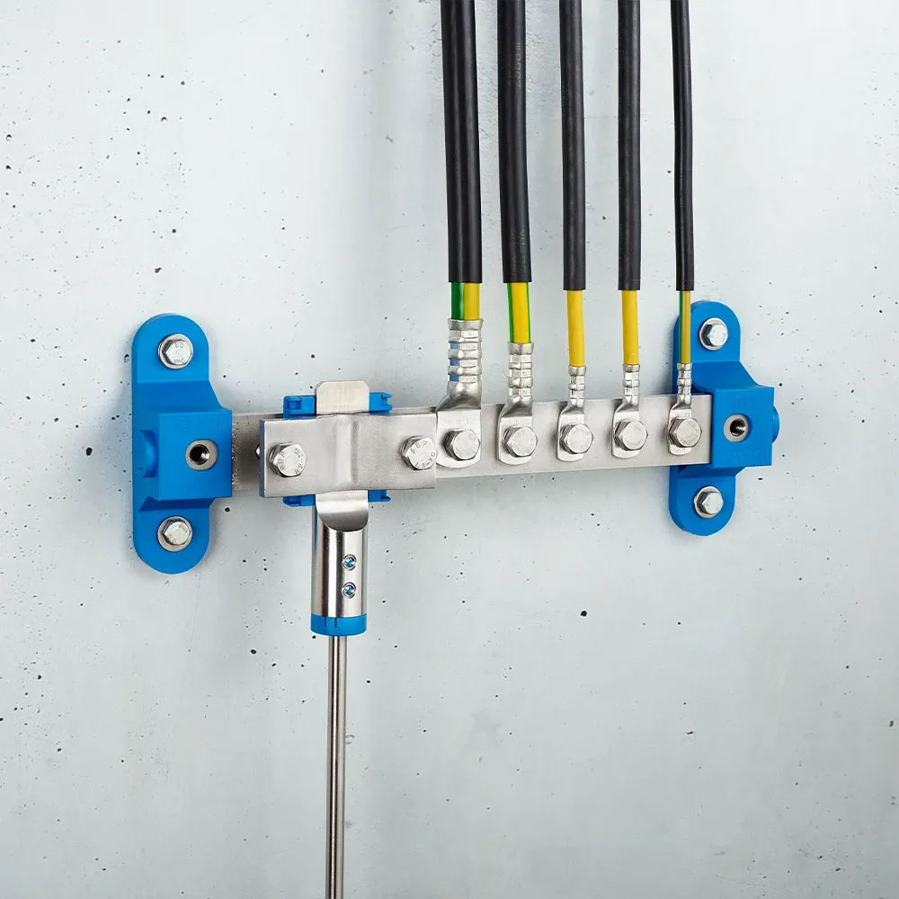 Wall-mounted grounding bar with metal clamps, connected black and yellow-green cables, and blue mounting brackets on a light gray wall.