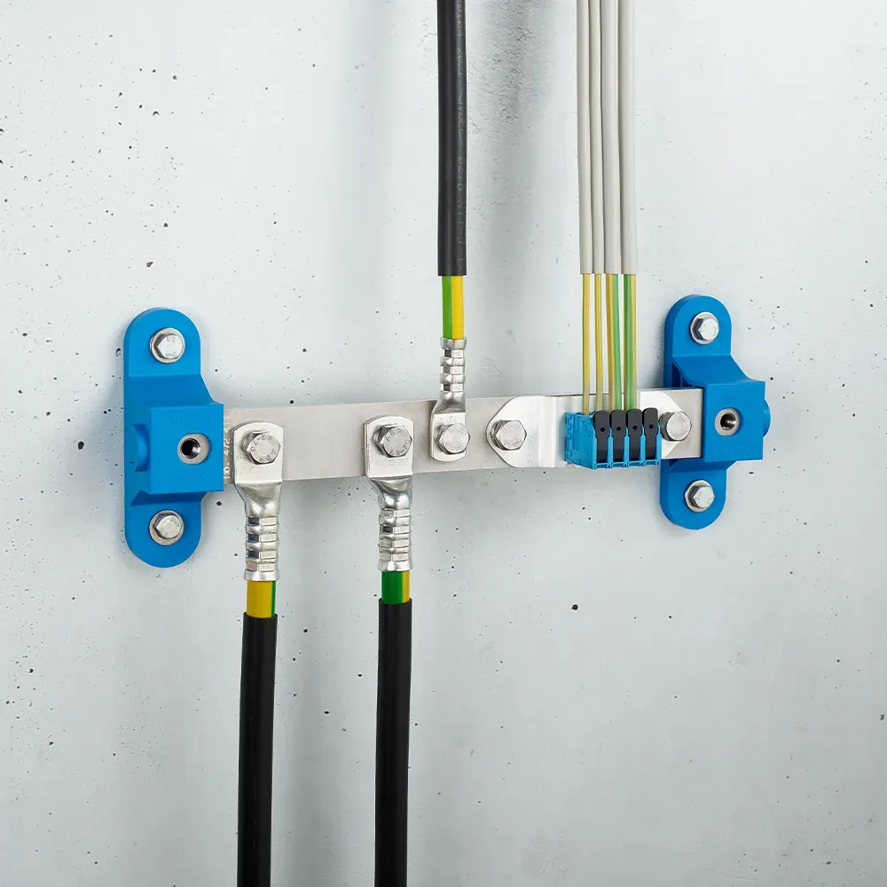 Wall-mounted grounding bar with metal terminals and connected black and yellow-green cables on a light gray wall.