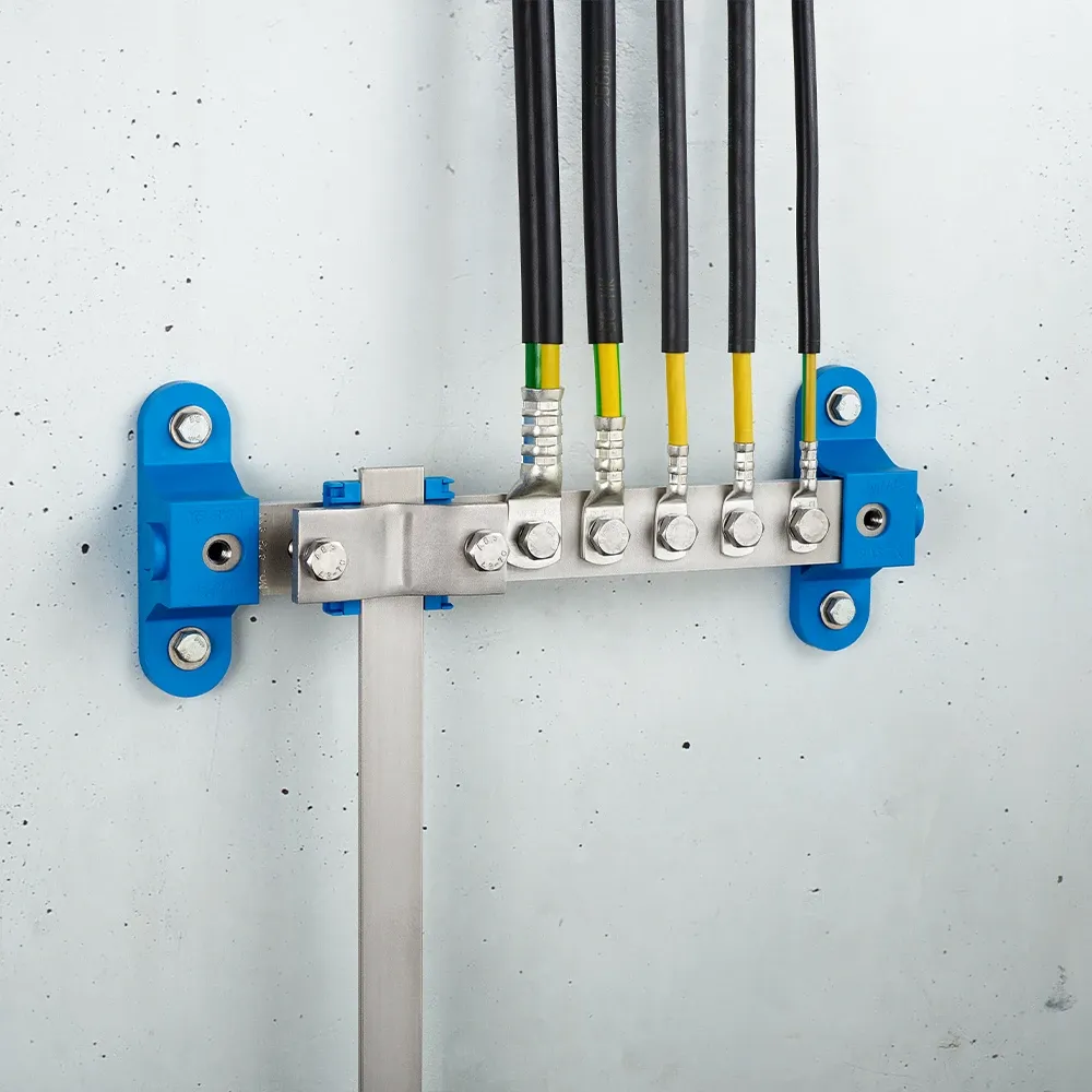 Wall-mounted grounding bar with metal clamps, connected black and yellow-green cables, and blue mounting brackets on a light gray wall.