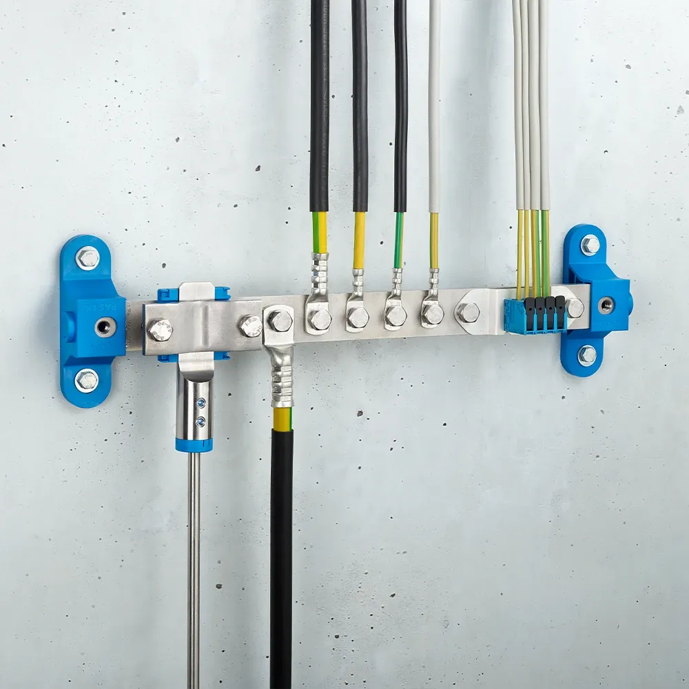 Wall-mounted grounding bar with metal terminals, connected black and yellow-green cables, and blue mounting brackets on a light gray wall.