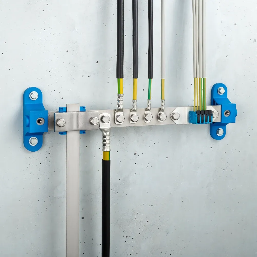 Wall-mounted grounding bar with metal terminals, connected black and yellow-green cables, and blue mounting brackets on a light gray wall.
