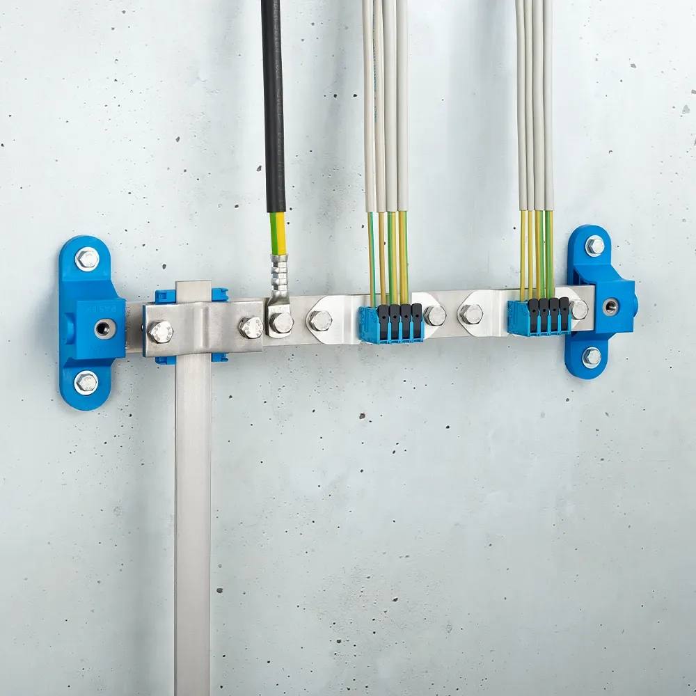 Wall-mounted grounding bar with metal terminals, connected black and yellow-green cables, and blue mounting brackets on a light gray wall.