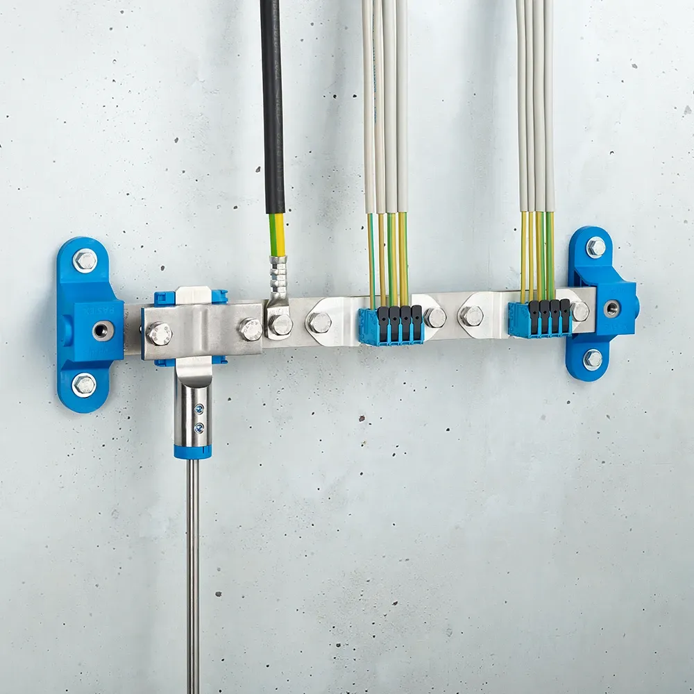 Wall-mounted grounding bar with metal clamps, connected black and yellow-green cables, and blue mounting brackets on a light gray wall.