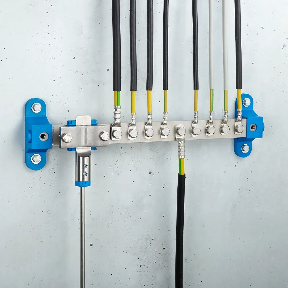Wall-mounted grounding bar with metal terminals, connected black and yellow-green cables, and blue mounting brackets on a light gray wall.