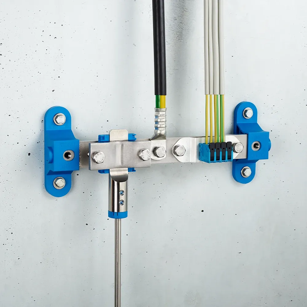 Wall-mounted grounding bar with metal clamps, connected black and yellow-green cables, and blue mounting brackets on a light gray wall.