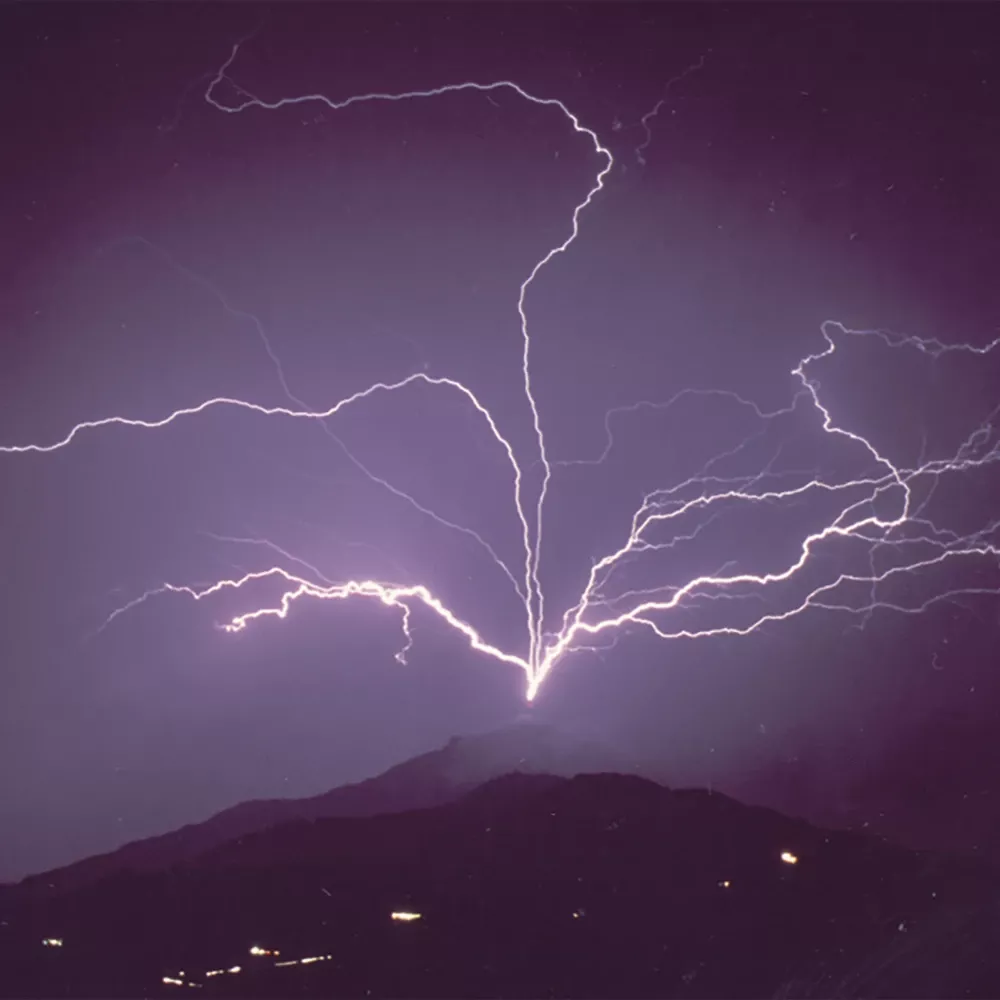 Multiple lightning bolts branching upward from a mountain peak into a dark purple night sky.