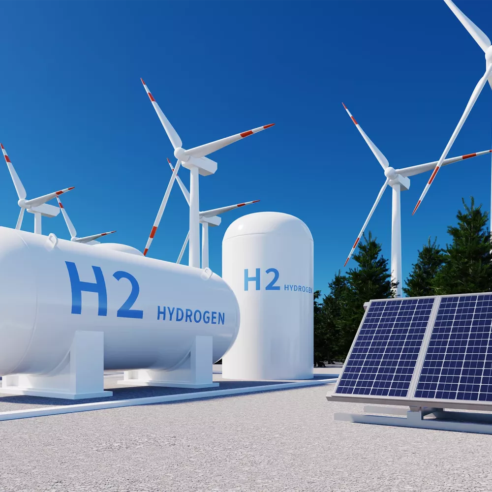 Hydrogen storage tanks labeled H2, wind turbines, and solar panels at a renewable energy facility under a clear blue sky.