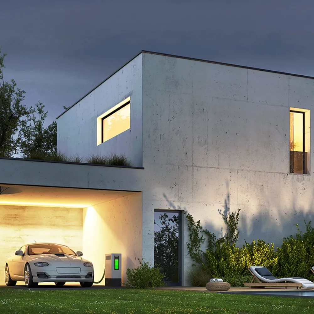Modern concrete house at dusk with illuminated windows, an electric car charging in the garage, garden lighting, and a pool in the foreground.
