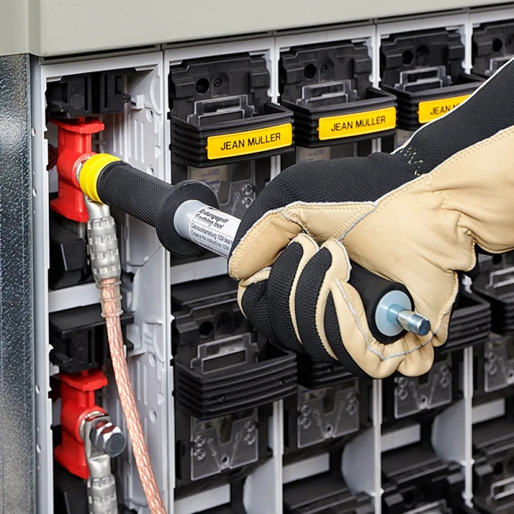 Close-up of a gloved technician connecting a grounding tool to a fuse switch in an electrical distribution cabinet with labeled modules.