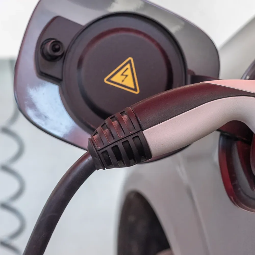 Close-up of an electric car charging connector plugged into the vehicle’s charging port, with a high-voltage warning symbol visible.