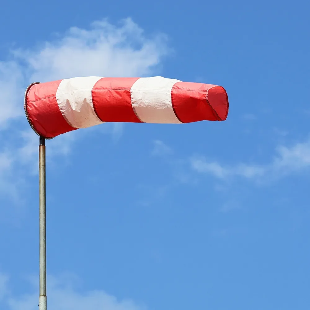 Red and white windsock on a pole against a blue sky with clouds.