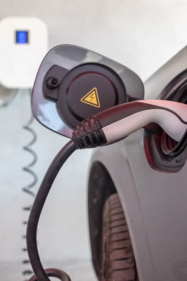 A captivating image displays a sleek electric car charging station, elegantly blending into its garage setting. The clean white wall and the contrasting black-and-white charging cable with a yellow triangle stand out, reflecting modern design and functionality.