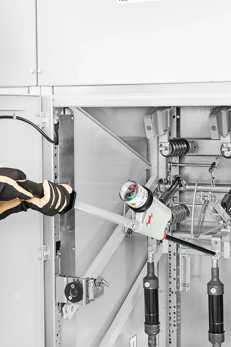 Un homme en tenue de protection tient un détecteur de tension à deux mains et vérifie des connexions haute tension.