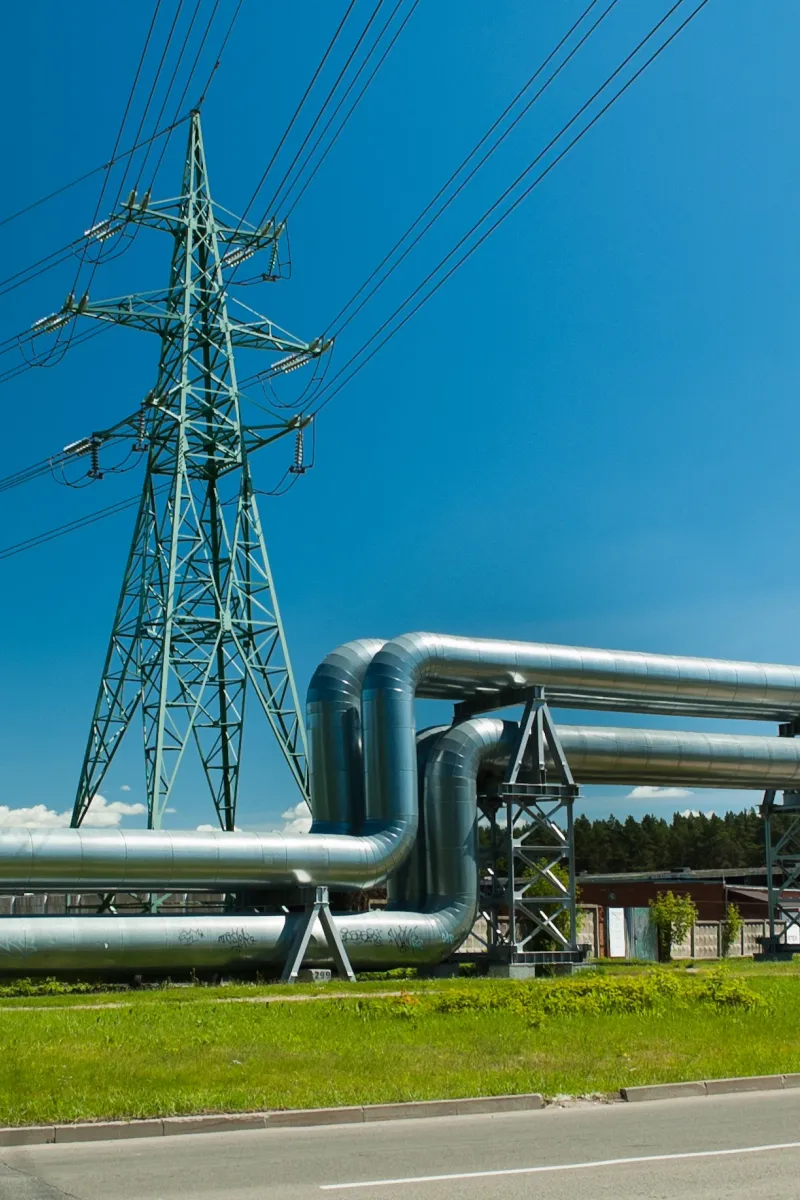 Ligne à haute tension et pipeline dans une prairie verte, sur fond de ciel bleu.