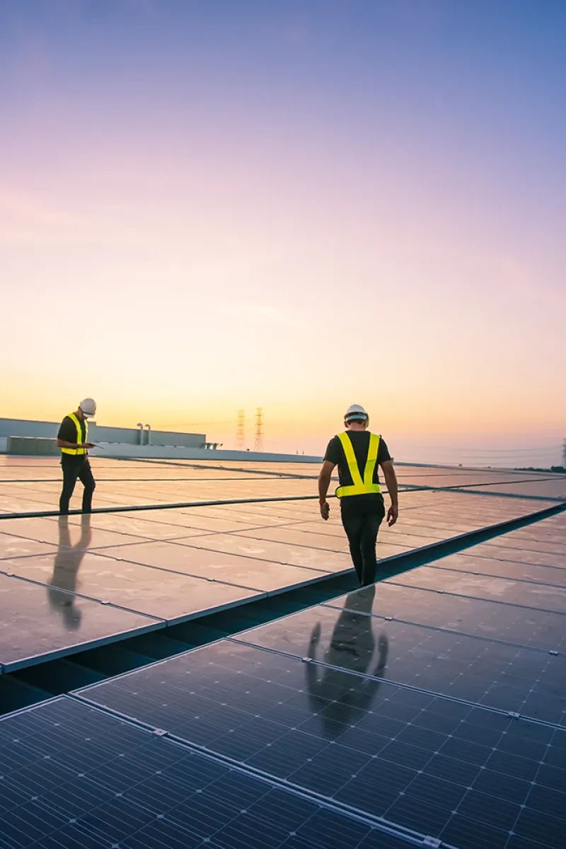 Two people on a flat rooftop with photovoltaic system. Sunset in the background.