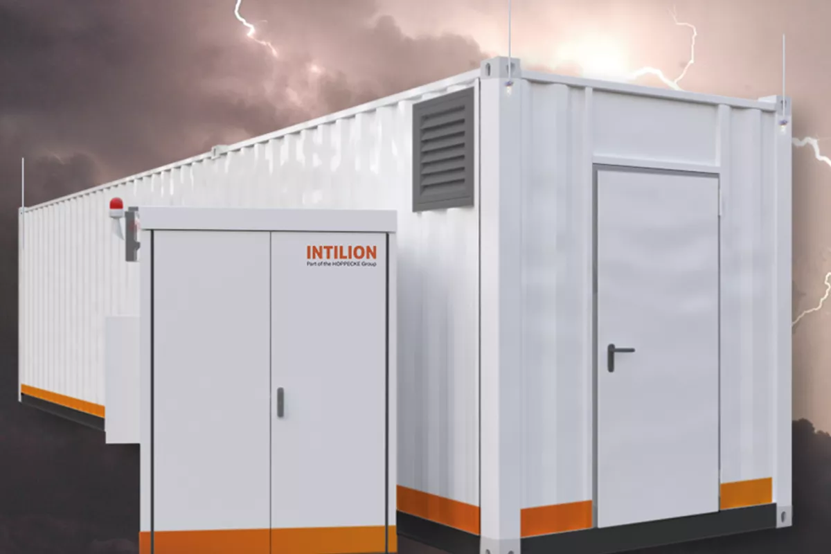 Modular, white, containerized power unit with orange accents, alongside a smaller control panel, against a backdrop of stormy weather with lightning.