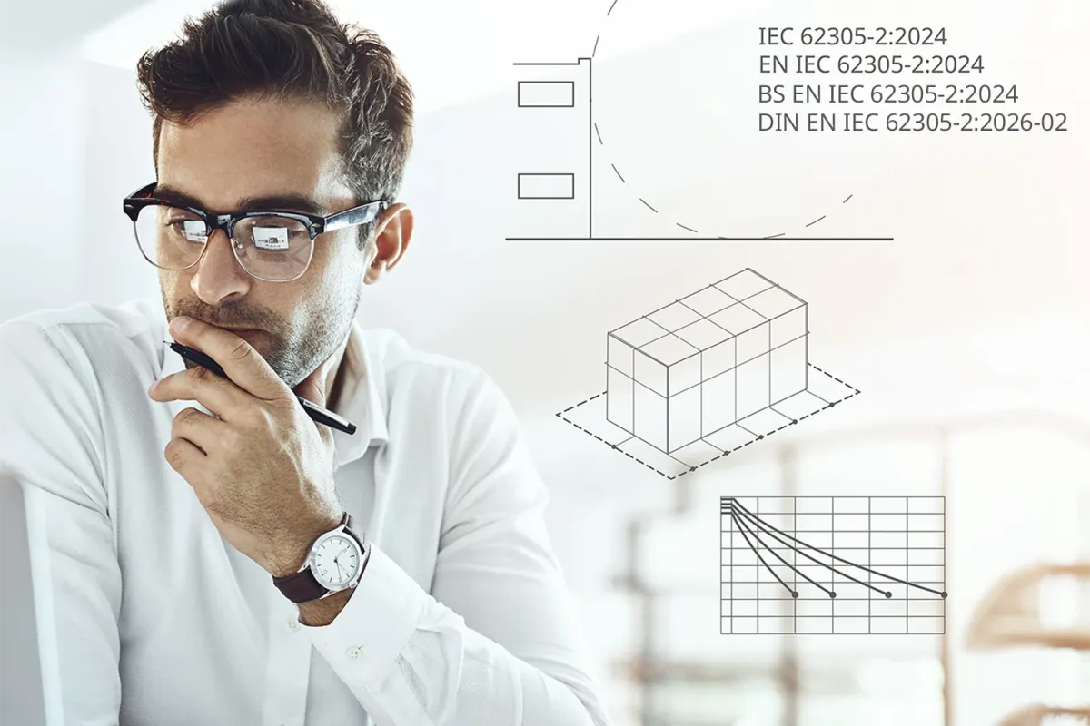 Man in glasses working at a laptop, holding a pen thoughtfully, with technical diagrams and IEC 62305-2:2024 graphics overlaid in the background.